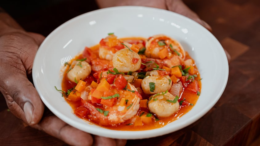 Des crevettes et des pétoncles recouverts de légumes et de sauce dans un bol.