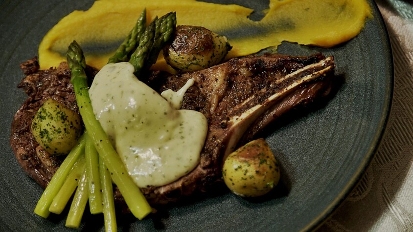 Un morceau d'entrecôte de bison recouvert de sauce et de légumes.