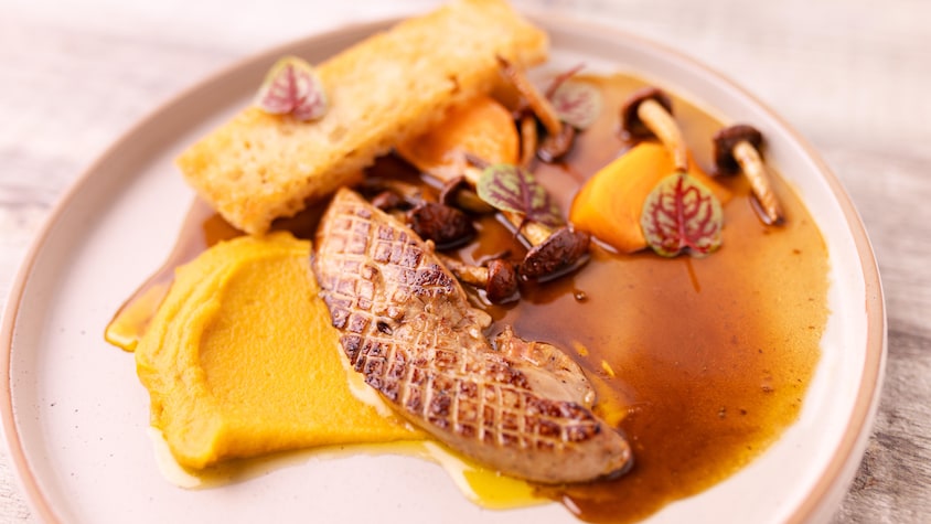 Du foie gras dans une assiette avec des morceaux de kakis et des girolles, le tout recouvert de jus au poivre des dunes.