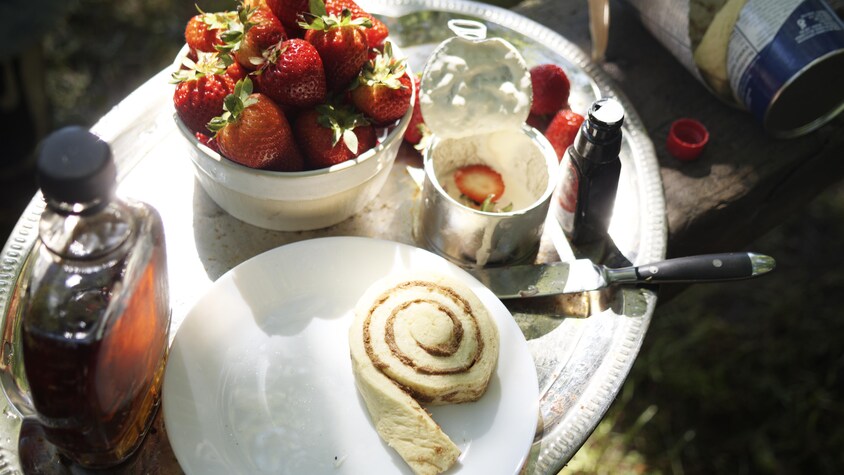 Dans un plateau de service, il y a un morceau de pâte à brioche, un pot de trempette chaude ainsi qu'un plat de fraises.