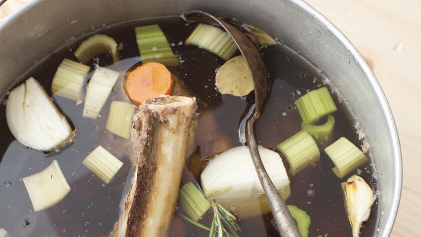 Une marmite contenant du bouillon, un os de gibier et des légumes.