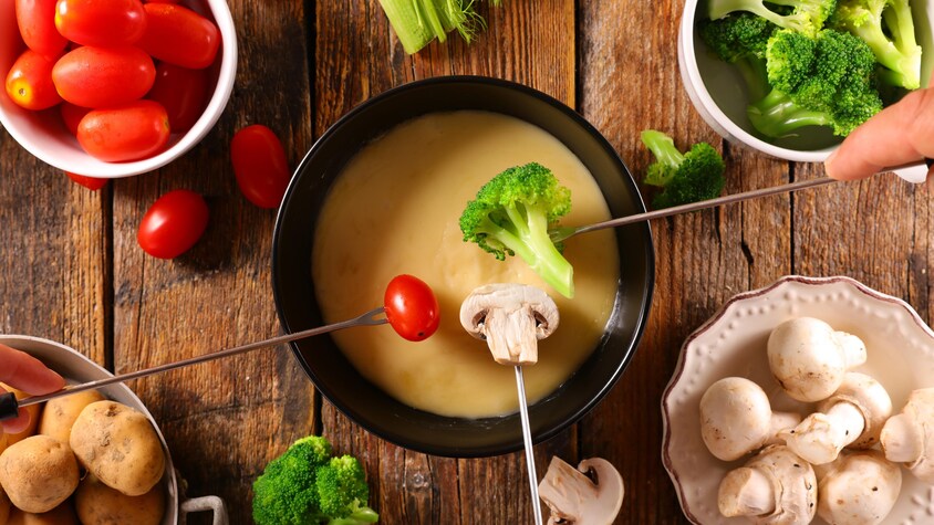 Un bol rempli de fondue au fromage avec des brocolis, des pommes de terre, des champignons et des petites tomates dans des bol à part.