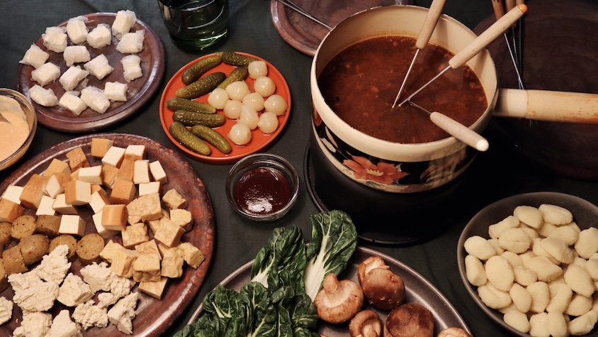 Un caquelon rempli de bouillon à fondue, avec plusieurs aliments à tremper dans le bouillon tels que : des champignons, du tofu, du tempeh, des gnocchis et des bok choys.