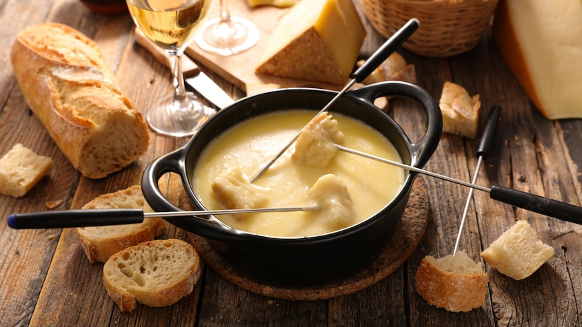 Une fondue au fromage avec deux verres de vin blanc et du pain baguette.