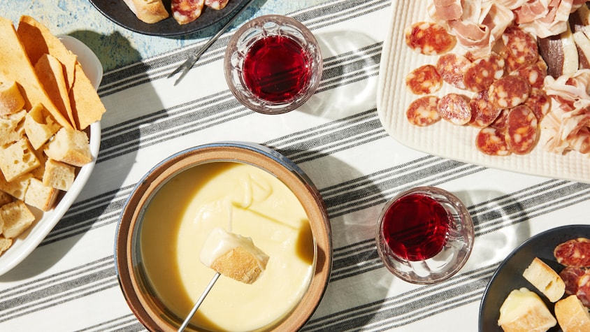 Une casserole de fondue au fromage accompagnée de plats de charcuteries.