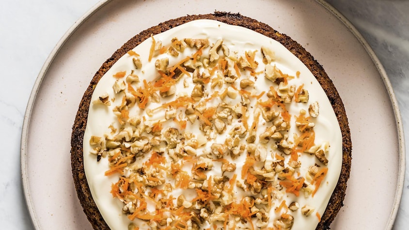 Un gâteau avec du glaçage à la vanille et garni de noix de Grenoble et de carotte râpée.