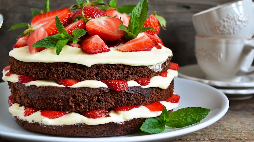 Un gâteau à étages contenant de la crème fouettée, des morceaux de fraises et des disques de gâteau au chocolat.