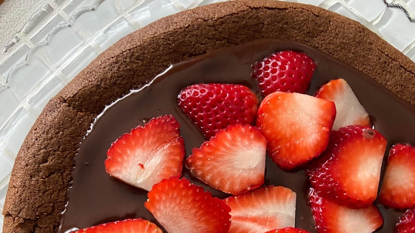 Un gâteau au chocolat sans farine garni de ganache au chocolat et de tranches de fraises.