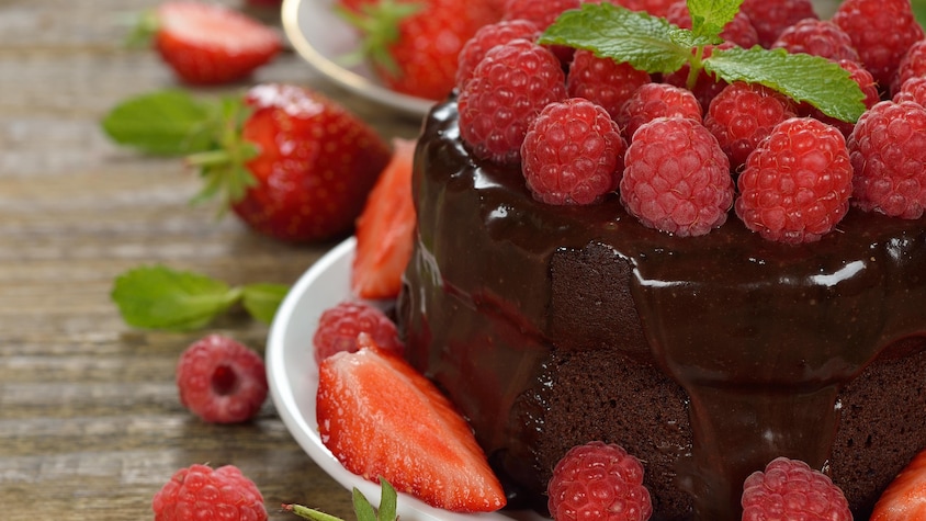 Un gâteau mi-cuit au chocolat nappé d'un crémage au chocolat coulant et décoré de framboises et fraises fraîches.