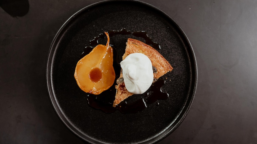 Une pointe de gâteau recouverte de crème fouettée et accompagnée d'une poire rôtie à l'érable.