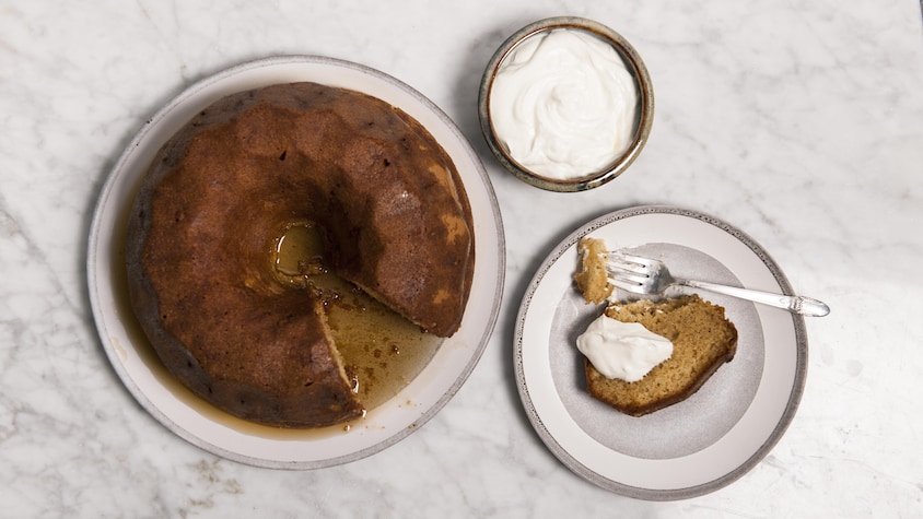 Un part de gâteau à l'érable et au whisky, servi aux côtés du gâteau entier et d'un bol de crème fouettée.