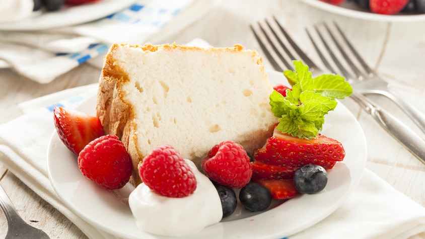 Une portion de gâteau servie avec des fruits frais et de la crème fouettée.