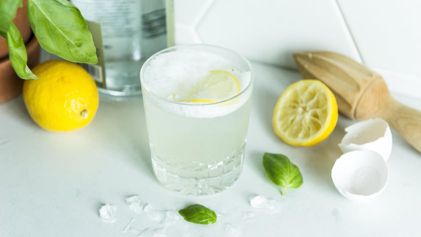 Une personne verse un gin citron-basilic sour dans un verre.