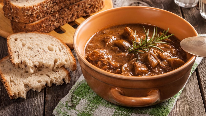 Un bol contenant du ragout de bœuf (goulache) accompagné d'une tranche de pain.