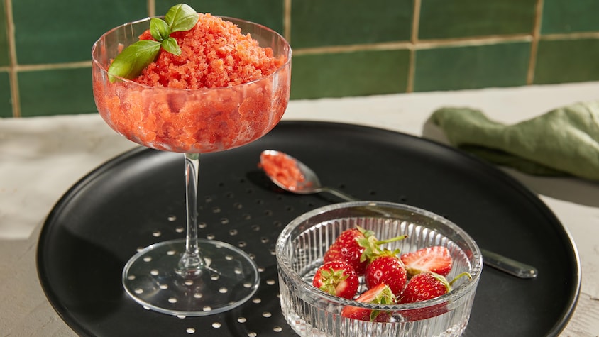 Une coupe remplie de granité aux fraises garnie de feuilles de basilic.