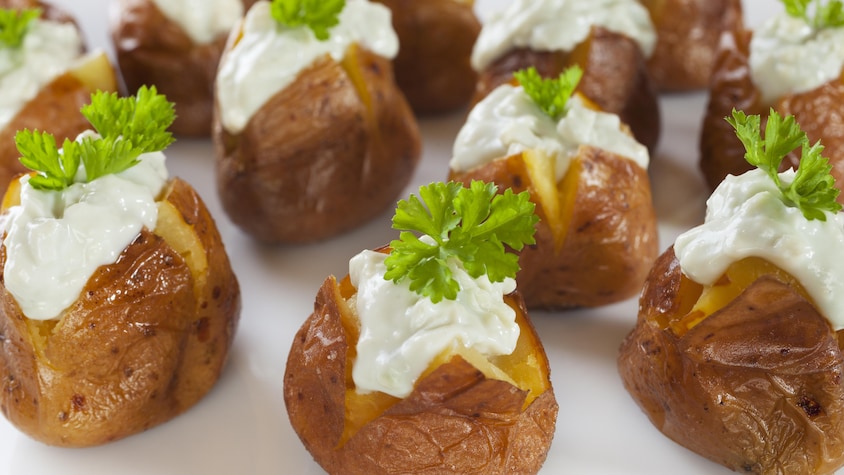 Plusieurs petites pommes de terre garnies de fromage.