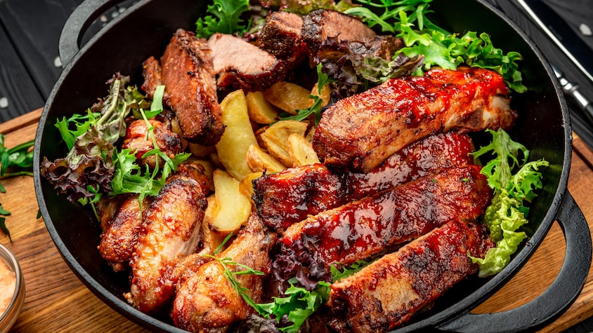 Un plat contenant des pommes de terres à la portugaise, des pilons de poulet et des morceaux d'agneau. La viande est couverte de sauce BBQ aux mangues.