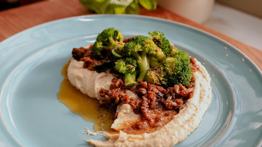 Une assiette contenant du hummus garni de brocolis et de lentilles, le tout nappé de beurre parfumé.