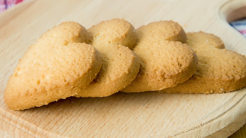Quatre biscuits sablés en forme de coeur disposés sur une planche en bois.