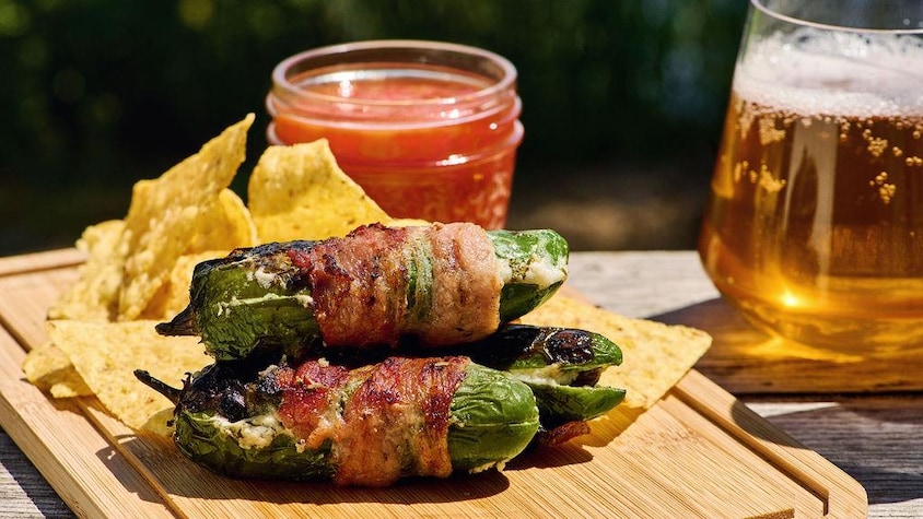 Des jalapeños farcis sur une petit planche de bois avec des chips, de la salsa et une bière.