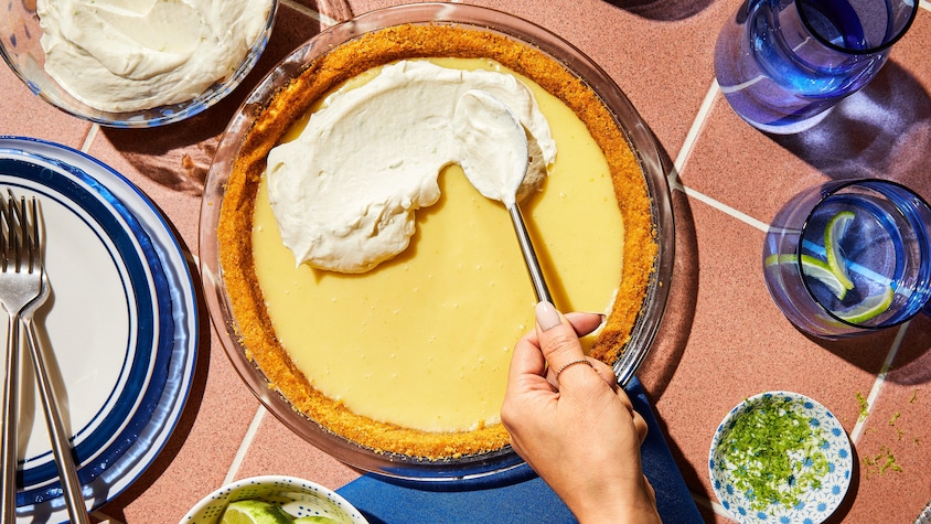 Une personne étend de la crème fouettée sur une tarte à la lime.