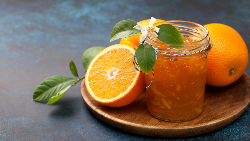 Un pot de marmelade d'orange dans un pot en verre, entouré d'une moitié d'orange et de deux oranges entières.