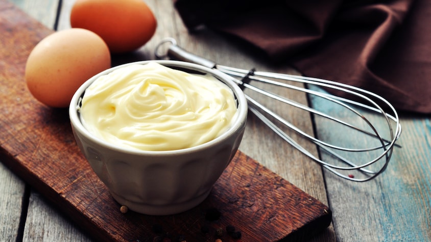 De la mayonnaise dans un bol avec des œufs à côté.
