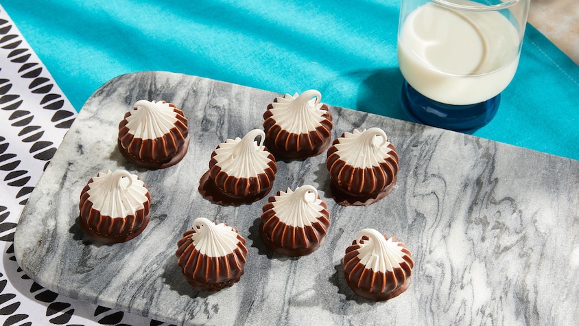 Des meringues trempées dans le chocolat sur une planche à découper.