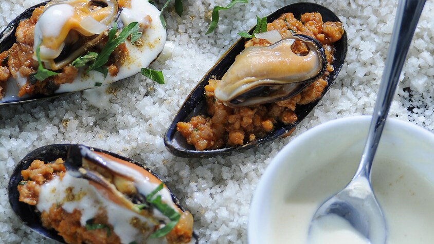 Des moules farcies sur un lit de gros sel.