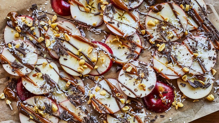 Tranches de pommes sur une plaque garnies de filets de caramel et de chocolat.