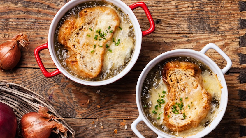 Deux bols de soupe à l'oignon recouverts d'un croûton de pain et de fromage fondu sur une planche de bois, vus de haut.