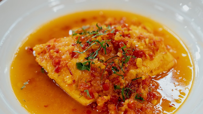 De l'omble de l'Arctique poché dans une assiette avec une sauce à la tomate et au safran. 