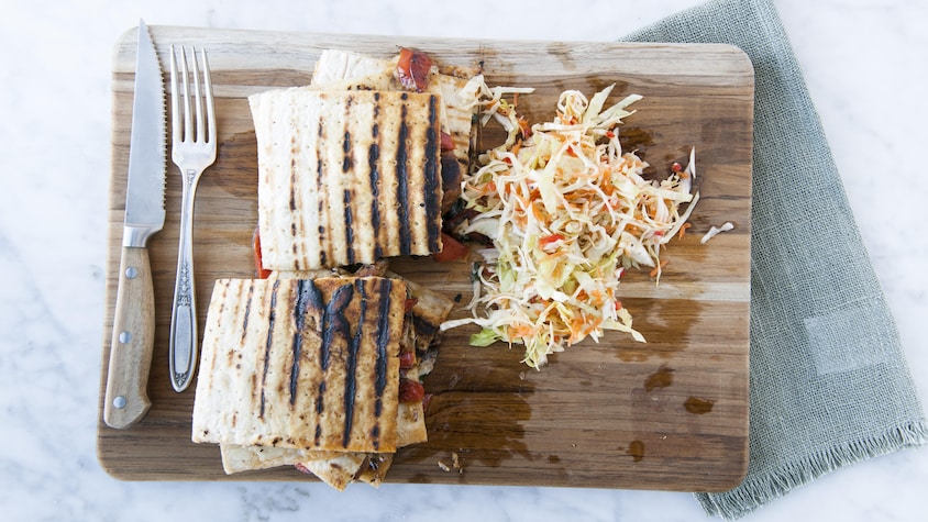 Deux parts de panini servies sur une planche de bois avec des ustensiles et accompagnées de salade de chou.