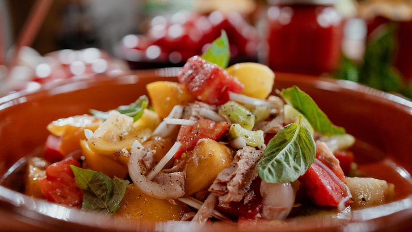 Une salade style panzanella au thon et aux tomates garnie de feuilles de basilic.