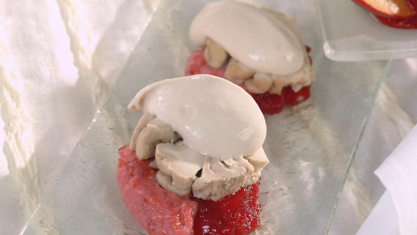 Deux boules de sorbet rose foncé recouvertes d'une tranche de cervelle de veau et d'une quenelle de crème sure, dans une assiette en verre.  