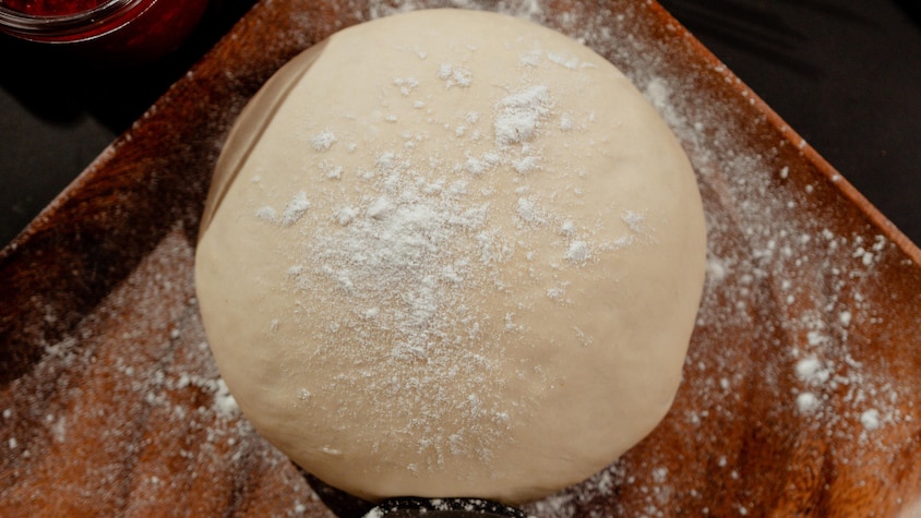 Un boule de pâte recouverte de farine dans une assiette en bois.