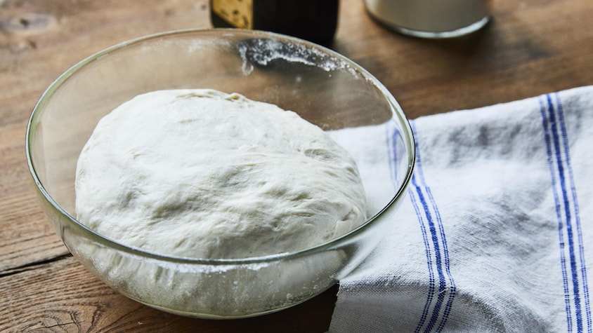 Un bol contenant la pâte à pizza crue sur un comptoir. 
