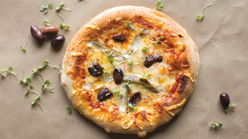 Une pizza garnie de fromage d'olives calamata et de filets de poisson avec la peau.