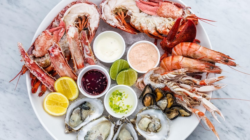 Un plateau avec du homard, du crabe, des huîtres, des moules et des crevettes servis sur glace, avec des sauces et des tranches d'agrumes.