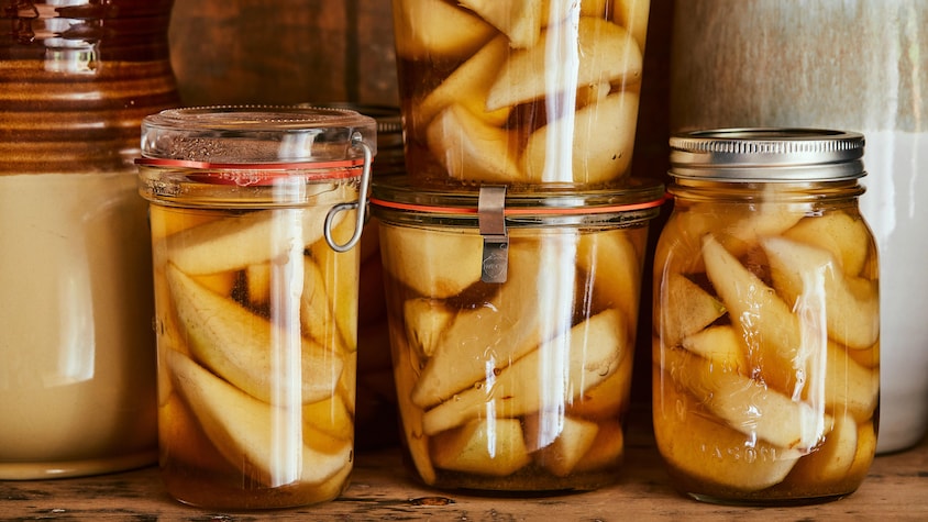 Il est possible de voir 4 conserves de poires pochées à l'érable et au mélilot sur une étagère en bois.