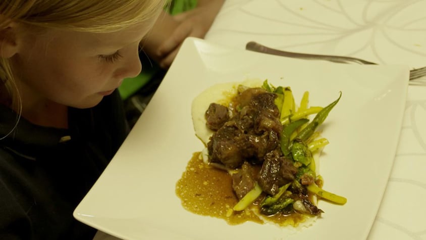 Une assiette de poitrine de porc croustillante et de légumes déposée sur une table devant un enfant.