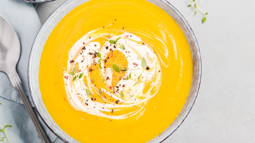 Un potage à la courge décoré de pousses et de crème.