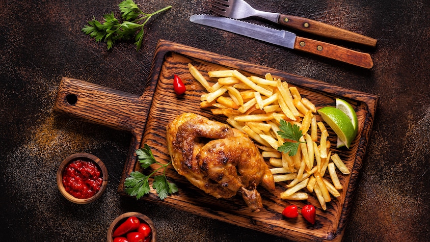 Du poulet piri-piri en demi-crapaudine servi sur une planche, avec des frites et des quartiers de lime.