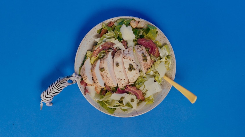 Une poitrine de poulet sur une salade césar dans un bol.