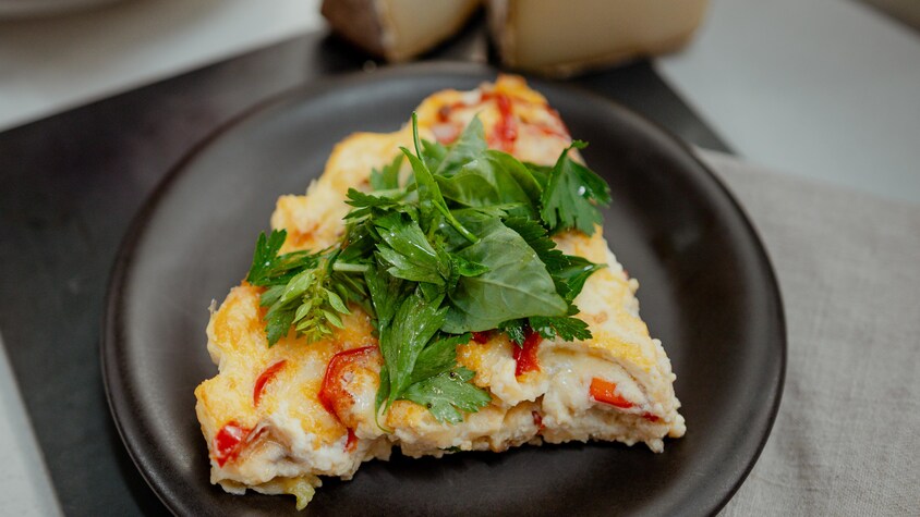 Une pointe de quiche aux légumes sans croûte dans une assiette noire.