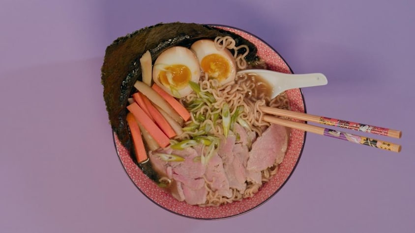 Un bol de soupe ramen au porc, servi avec des oeufs cuits dur, des carottes marinées et une feuille de nori.