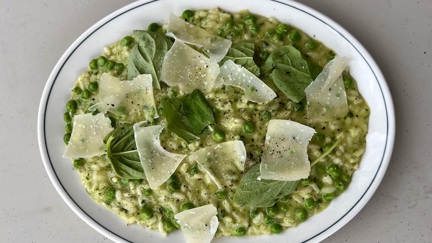 Un plat de risotto vert au basilic et à la roquette servi avec des petits pois et des copeaux de parmesan.