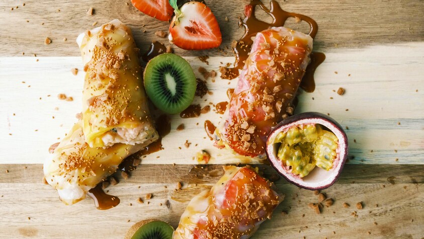 Des rouleaux de printemps sucrés sont servis avec des fruits sur une planche à découper.