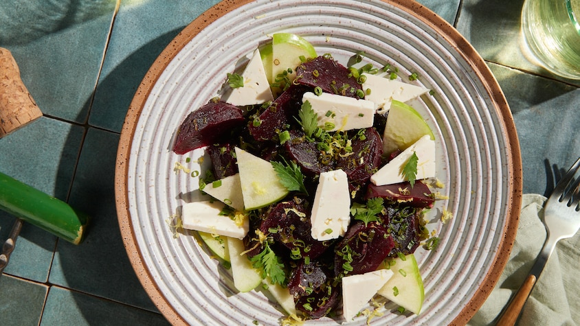 Dans une assiette, des morceaux de betteraves, de fromage féta et de pomme verte parsemés de fines herbes.