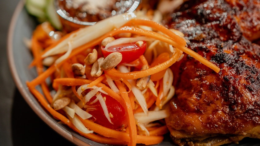 Un peu de salade de papaye épicée avec du poulet grillé dans une assiette.